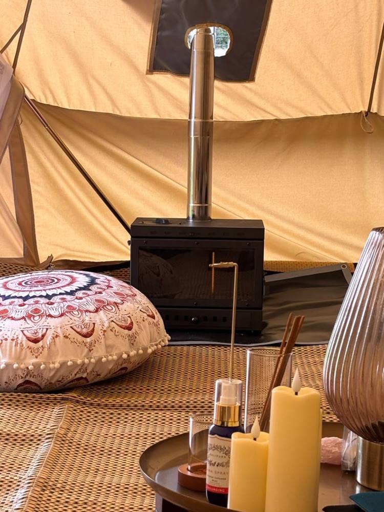 Inside the bell tent: a log burner, candles and floor cushions.