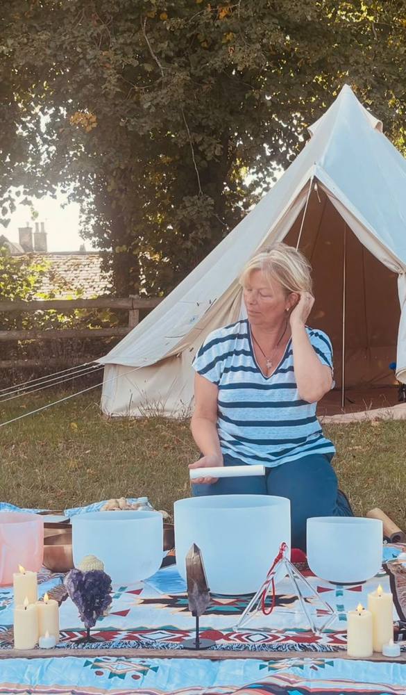A woman playing crystal singing bowls outdoors in front of a bell tent.