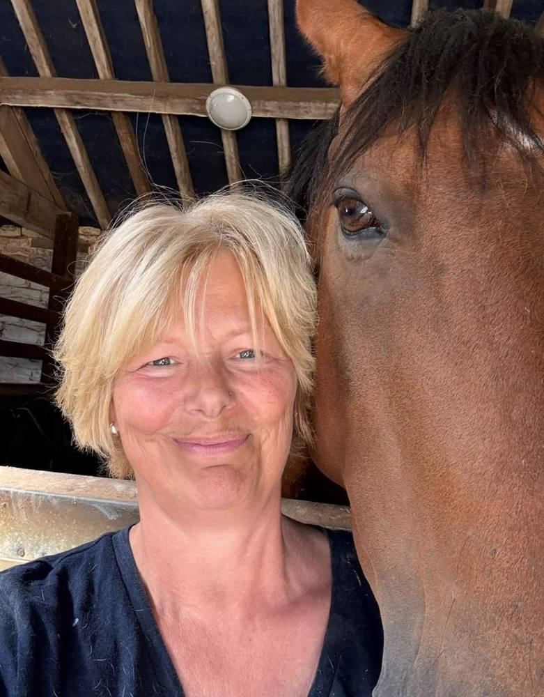 The founder of Nature, Horses & Holistics smiling beside a bay horse.